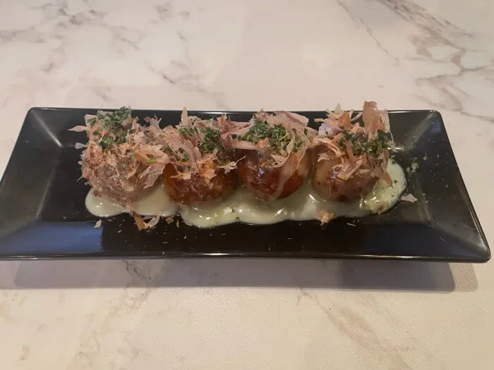 Takoyaki - Octopus balls topped with bonito flakes, green herbs, and drizzled with sauce at Ramen Jin, a Ramen restaurant in Houston